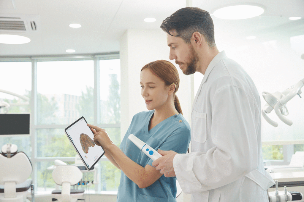 Dentist and dental assistant review a tablet showing a 3D dental model in a bright clinic.