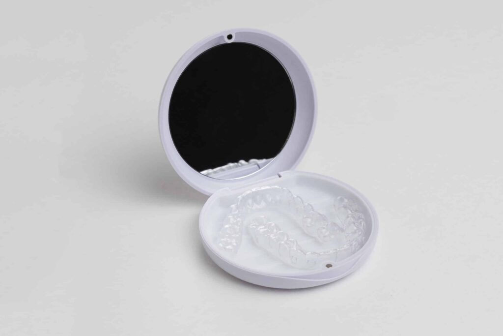 Open round white case with clear dental aligners laid inside on a light surface