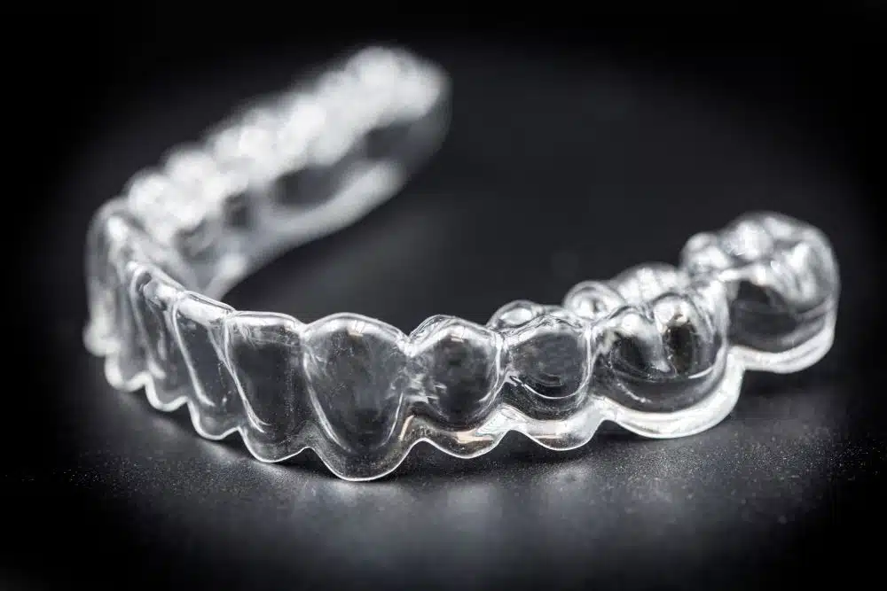 Clear dental aligner tray resting on a dark surface on a black background.”