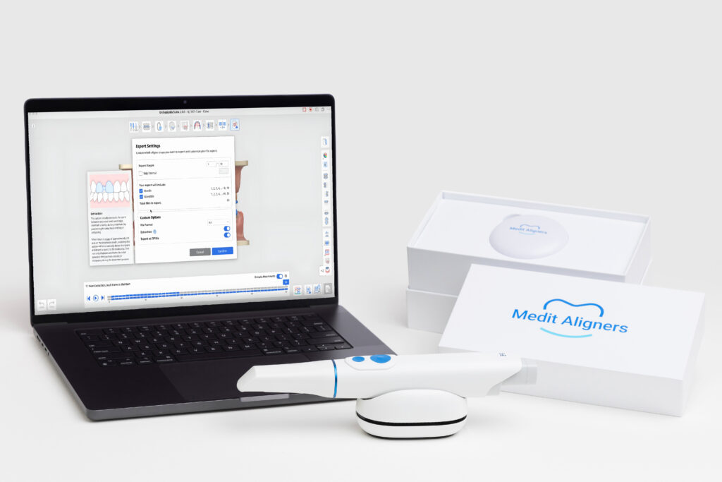 Laptop displaying dental alignment software on a white desk, with a white intraoral scanner in the foreground and a MediT Aligners box nearby.