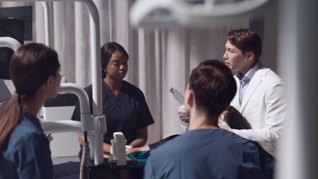 Medical team discusses a patient’s care around a bed with monitoring equipment in a hospital room.