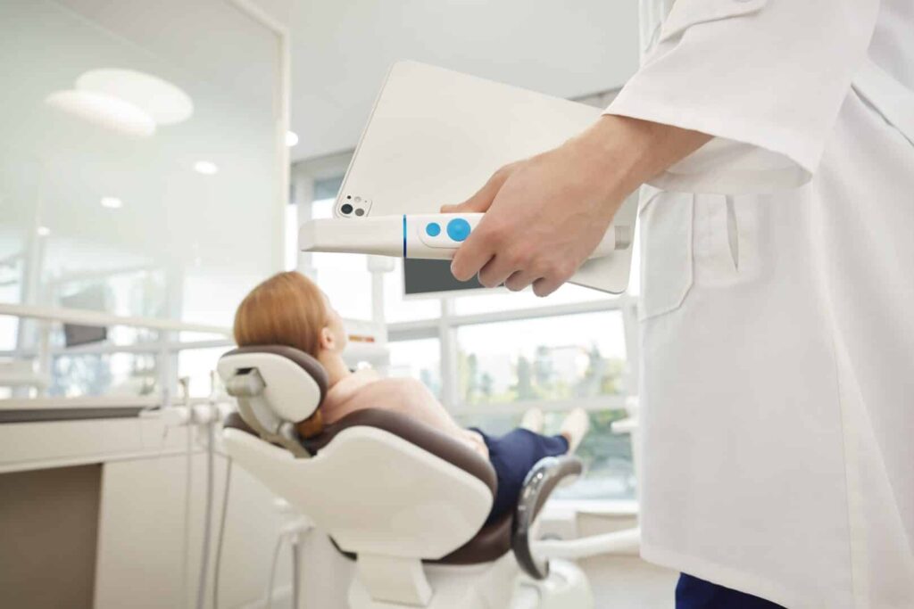 Dental professional using a handheld intraoral scanner over a patient in a reclining dental chair, capturing dental impressions